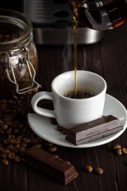 A cup of coffee with chocolates and coffee beans on a wooden table.