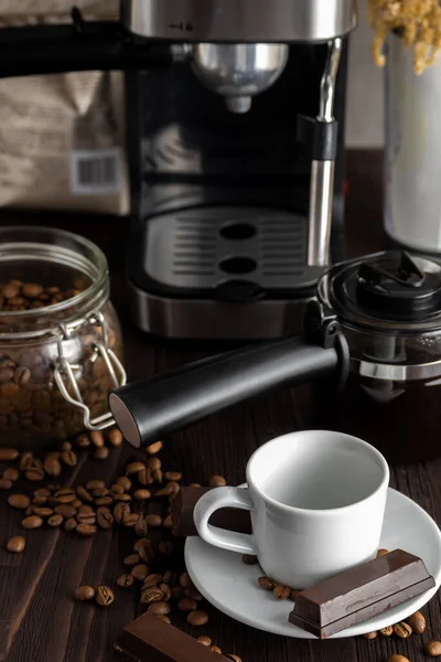 A cup of coffee with chocolates and coffee beans on a wooden table.