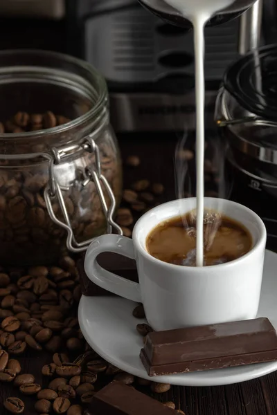 A cup of coffee with chocolates and coffee beans on a wooden table.