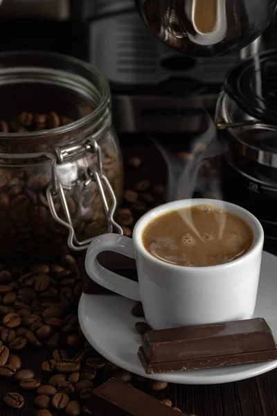 A cup of coffee with chocolates and coffee beans on a wooden table.