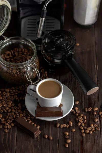 A cup of coffee with chocolates and coffee beans on a wooden table.