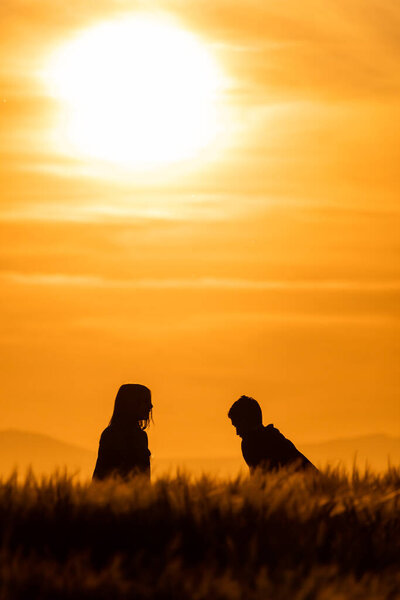 silhouettes of girl and boy in a cereal field at sunset with a sky of fire