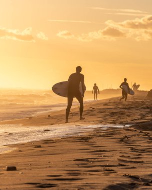 Altın gün batımında sahilde koşan sörfçüler