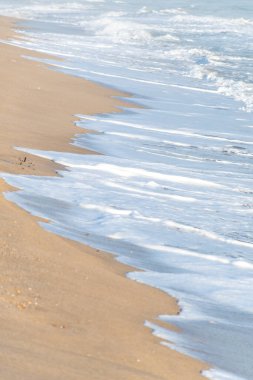 Dalgalar kumsalda kırılıyor ve beyaz köpük oluşturuyor.