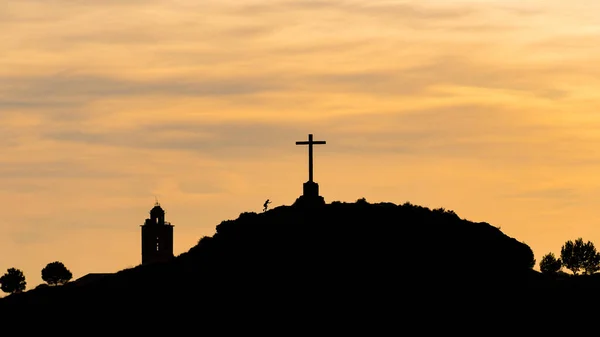 Tepenin tepesinde zıplayan ve koşan bir çocuğun silüeti büyük bir haç ve alacakaranlıkta bir kilise.