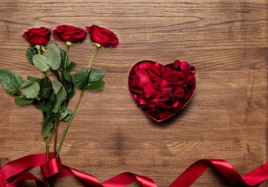 Güzel kırmızı kurdeleli kırmızı hediye kutusu ve ahşap arka planda izole güller.