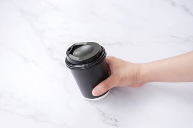 Genç bir kadın mermer masada siyah bir kahve fincanı tutuyor..