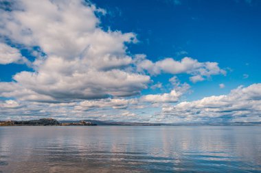 Parlak bulutlu gökyüzünün altında huzurlu göl manzarası
