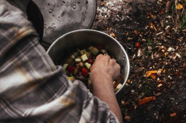 Sonbahar ormanında kamp ateşi iki kişi tarafından pişiriliyor. Bir tencerede sebze karıştıran kadın.