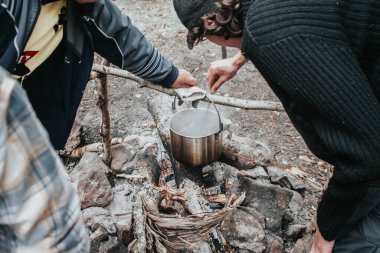 Sonbahar ormanında kamp ateşi iki kişi tarafından pişiriliyor.