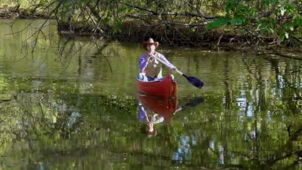 Ковбой в каноэ плавает по реке в лесу — стоковое видео