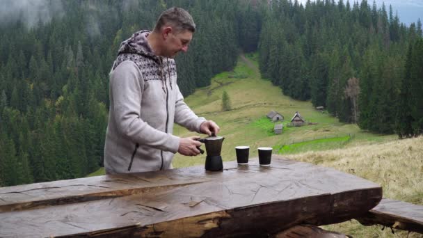 Мужчина наливает кофе из кофеварки утром в горах — стоковое видео