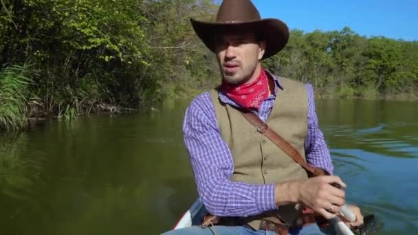 Ковбой в каноэ плавает по реке — стоковое видео