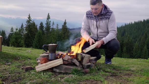 Egy férfi a tűz közelében a hegyekben. — Stock videók