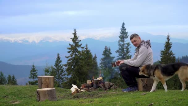 Чоловік з собакою біля багаття в горах — стокове відео