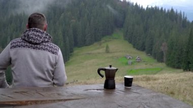 Bir adam kahve içer ve güzel manzaraya bakar. Kahve makinesi ve bardak masanın üstünde.