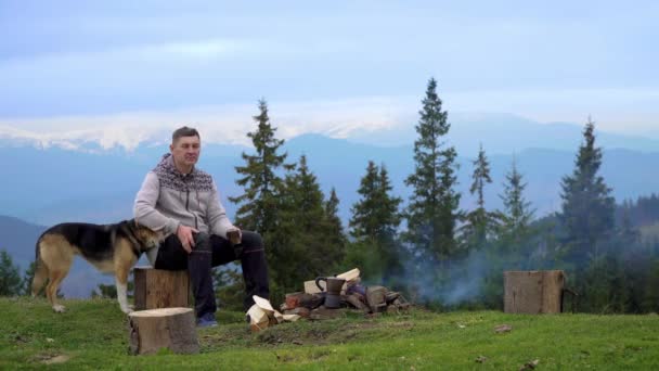 山の中で火の近くに犬を持つ男 — ストック動画