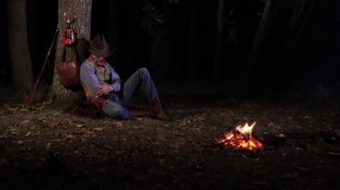 Geceleri ateşin yanında, ormanda bir kovboy.
