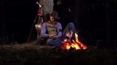 Geceleri ateşin yanında, ormanda bir kovboy.