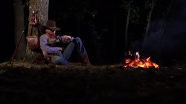 Geceleri ateşin yanında, ormanda bir kovboy.