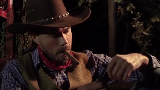 The cowboy smokes a cigar in the forest at night — Stock Video