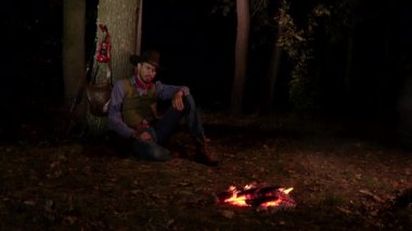 Geceleri ateşin yanında, ormanda bir kovboy.