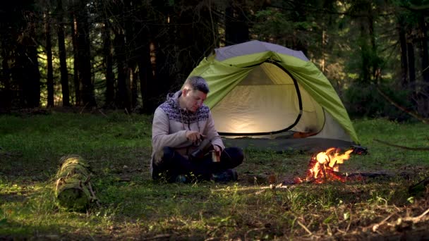 Um homem bebe café perto de uma tenda na floresta — Vídeo de Stock