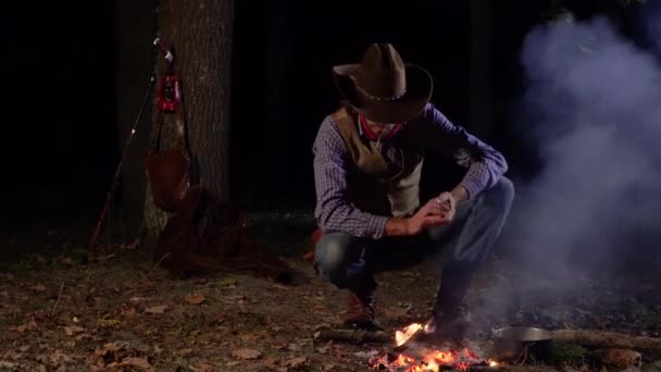 Cowboy perto do fogo na floresta à noite — Vídeo de Stock