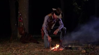 Geceleri ateşin yanında, ormanda bir kovboy.