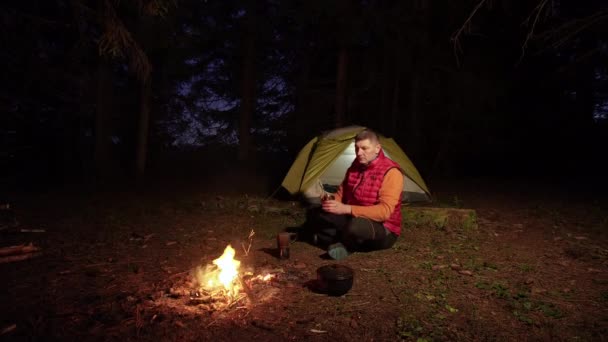 Um homem bebe café perto de uma fogueira — Vídeo de Stock