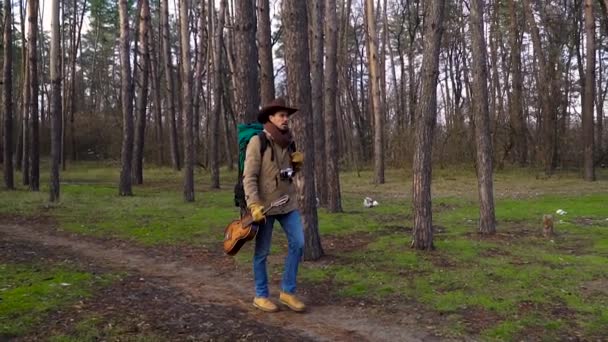 Ein Backpacker mit Gitarre und Kamera läuft auf einem Waldweg — Stockvideo