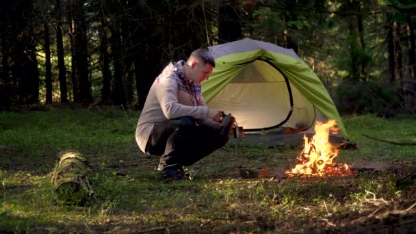 A man drinks coffee near a tent in the forest — Stock Video