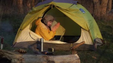 Genç bir adam ormandaki bir çadırda dizüstü bilgisayarda çalışıyor.