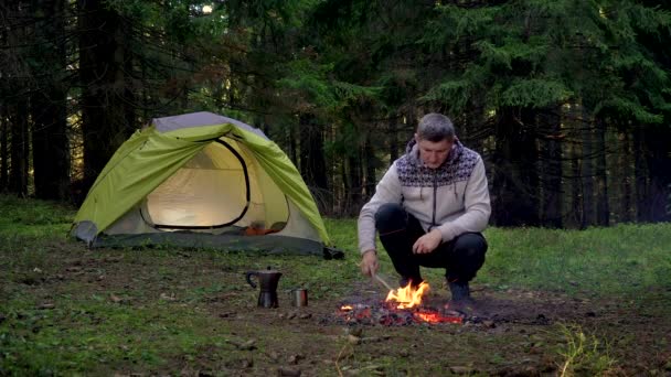 A man warms his hands over a fire in the forest — Stock Video