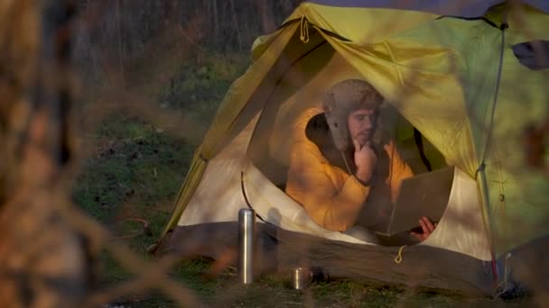 Ein junger Mann arbeitet an einem Laptop in einem Zelt im Wald — Stockvideo