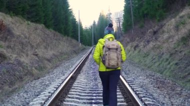 Sırt çantalı bir kadın demiryolunda yürüyor.
