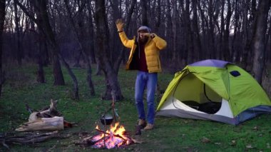 Komik adam ormanda çadır ve kamp ateşinin yanında dans ediyor.