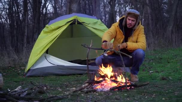 En man nära en lägereld och ett tält i skogen — Stockvideo