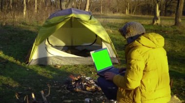 Ormandaki yangının yakınındaki dizüstü bilgisayarda çalışan genç bir adam.