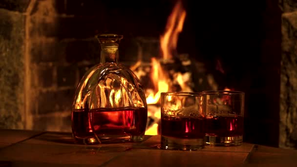 Μπουκάλι και ποτήρια με ουίσκι ή κονιάκ στο φόντο της φωτιάς στο τζάκι — Αρχείο Βίντεο