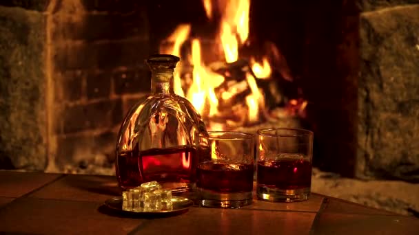 Bottle and glasses with whiskey or cognac on the background of fire in the fireplace — Stock Video