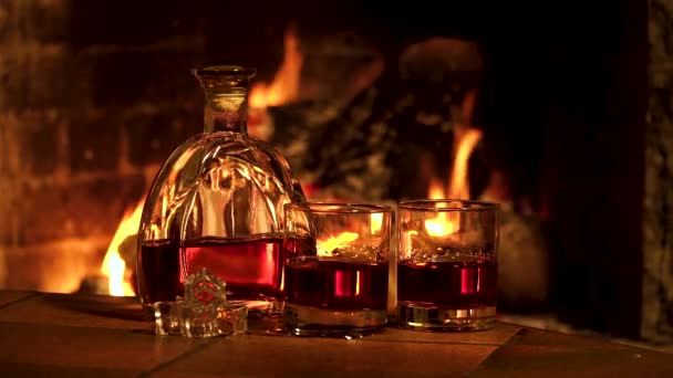 Flasche und Gläser mit Whiskey oder Cognac auf dem Hintergrund des Feuers im Kamin — Stockvideo