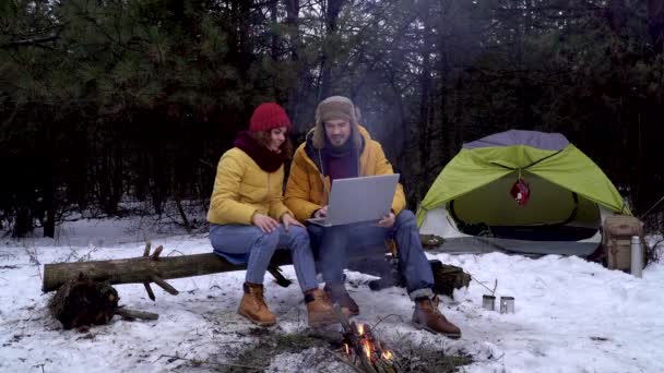 Парень и девушка с ноутбуком возле костра в зимнем лесу — стоковое видео