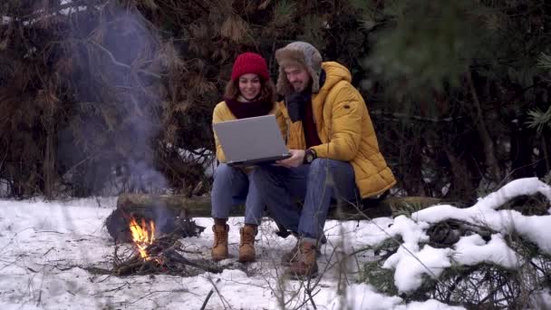 Парень и девушка с ноутбуком возле костра в зимнем лесу — стоковое видео