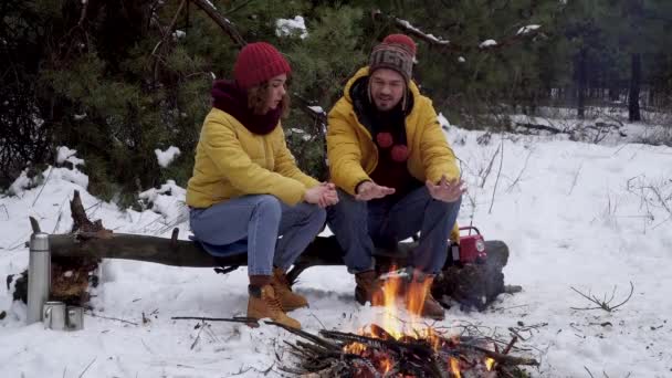 Молодой человек и женщина греют руки над костром в зимнем лесу — стоковое видео