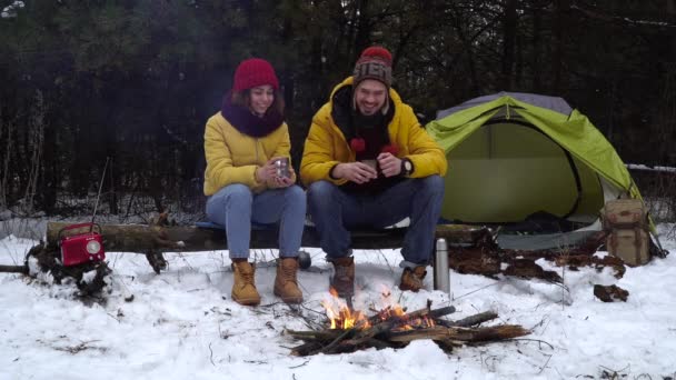 ชายหนุ่มและหญิงดื่มชาข้างไฟในป่าฤดูหนาว — วีดีโอสต็อก