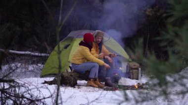 Genç adam ve kadın, kışın ormanda kamp ateşinin yanında.