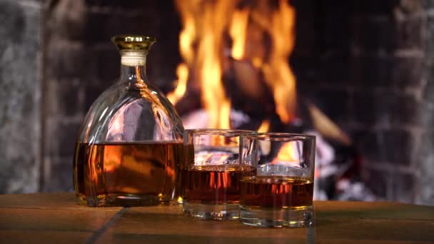 火堆中的火堆后面，装有威士忌或白兰地的酒瓶和玻璃杯 — 图库视频影像