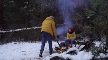 Genç adam ve kadın, kışın ormanda kamp ateşinin yanında.