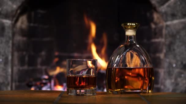 Botella y vaso con whisky o coñac en el fondo de fuego en la chimenea — Vídeo de stock